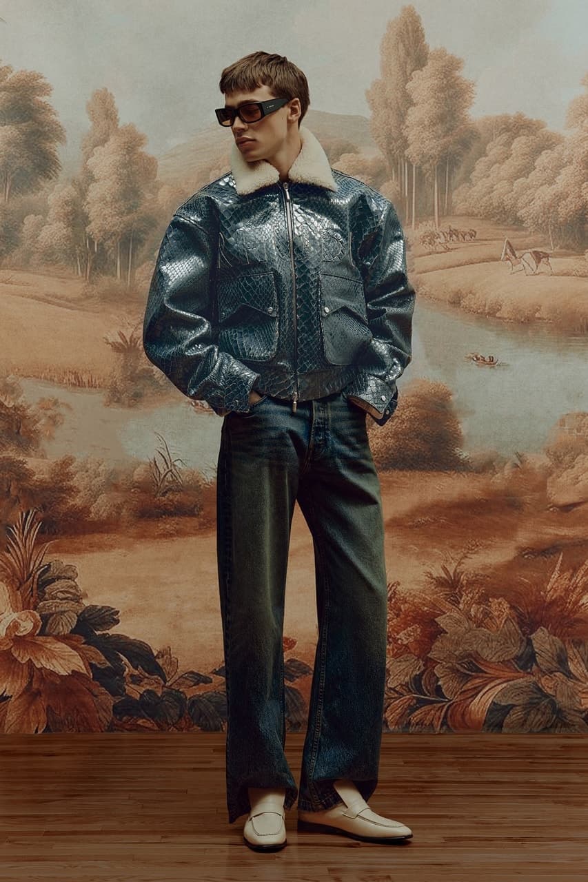 Model wearing a dark leather jacket and denim before a painted landscape